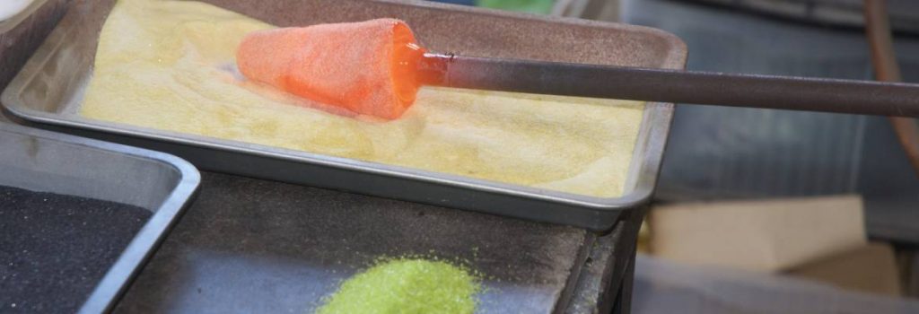Coloured glass chips and powders being added to hot glass on an iron
